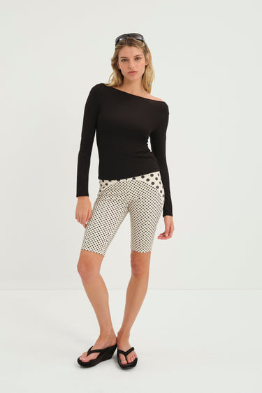 Woman wearing a black long-sleeve top and nude capri pants with black polka dot pattern on a white background