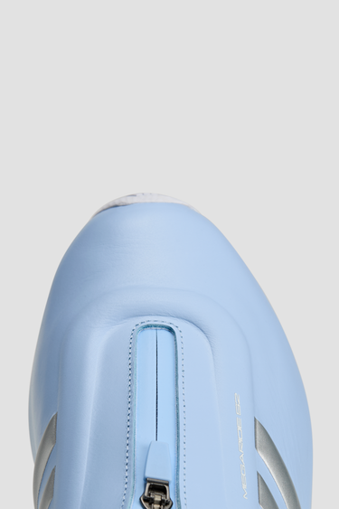 Light blue adidas athletic shoes with silver stripe white soles and a zipper tongue on a light gray background